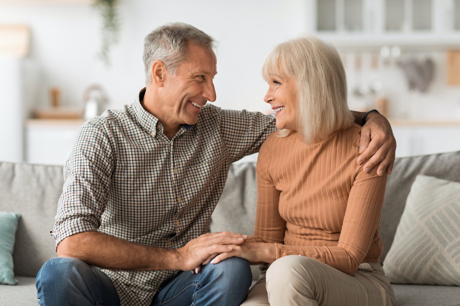 Happy Senior Couple Talking Embracing Sitting On Sofa At Home